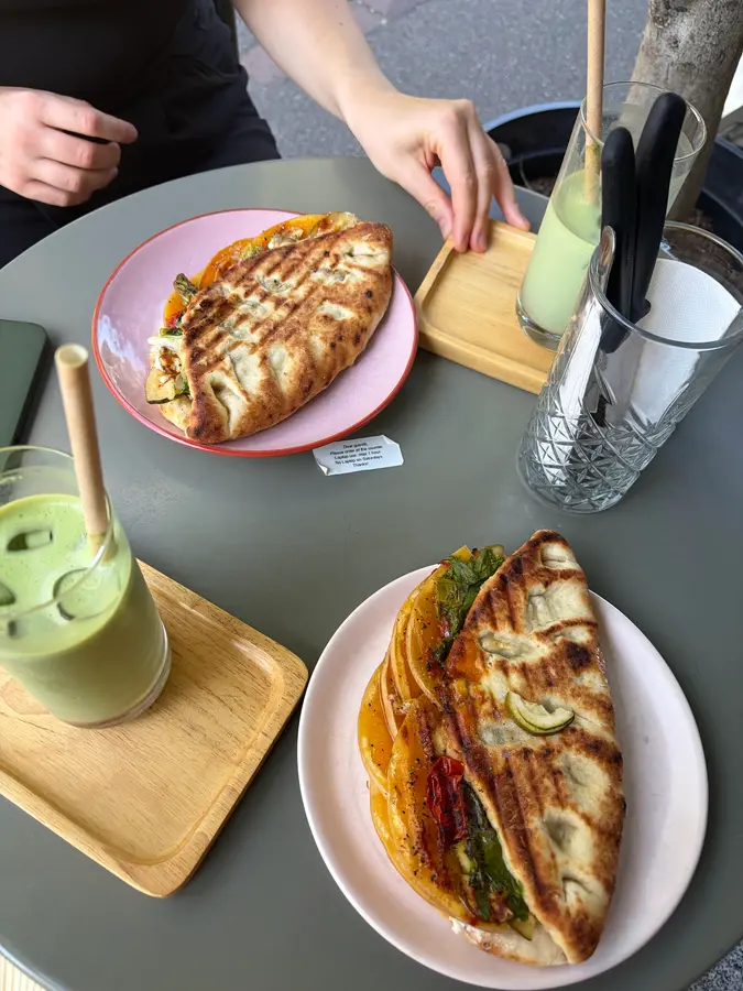 Zwei gegrillte Focaccia-Sandwiches auf rosa Tellern, dazu Matcha-Drinks